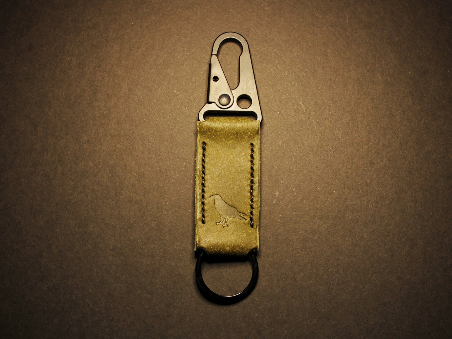 Green leather keychain with metal clip on a dark brown background