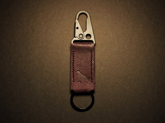 Purple leather keychain with metal clip on a dark brown background
