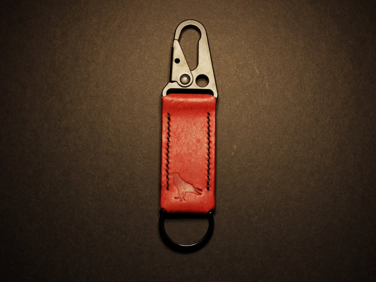 Red leather keychain with metal clip on a dark brown background