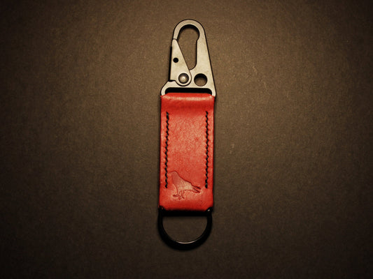 Red leather keychain with metal clip on a dark brown background